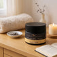 Jar of body butter on a wooden surface with a candle and book in the background